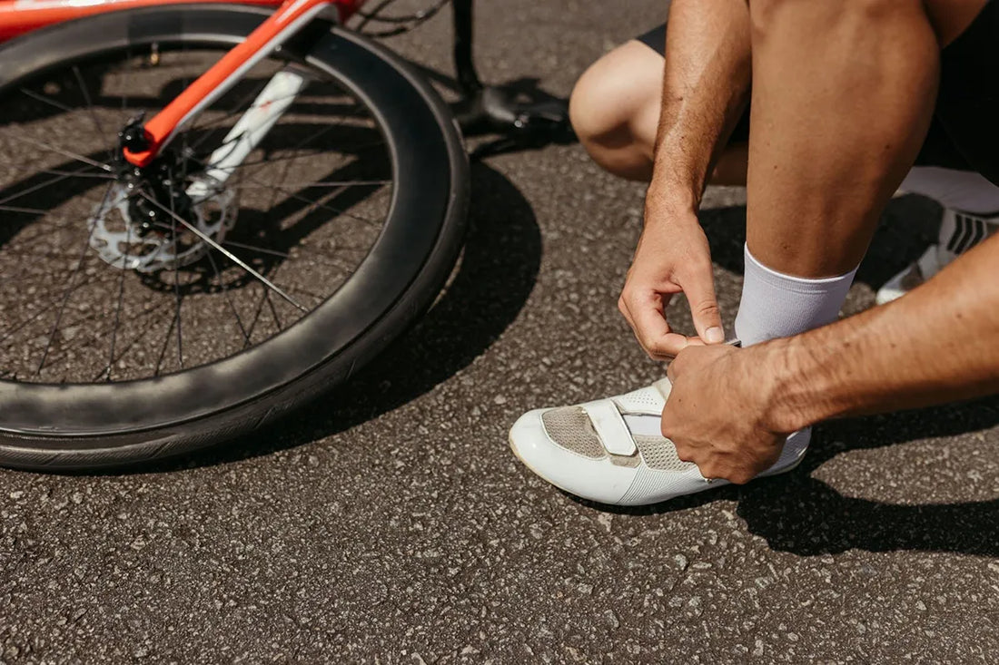 A cyclist laces up shoes next to a bike, ready for an outdoor journey.